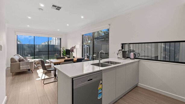 A modern kitchen with a dishwasher, a dining area with a table and chairs, and a sofa. - Campbelltown modern home Family Stay (Campbelltown)