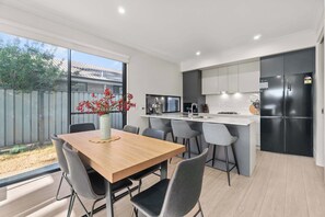 A modern kitchen with a dining area, featuring a wooden table, grey chairs, and a built-in island with a sink and stove.