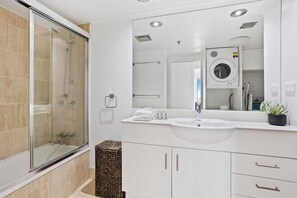 Ein modernes Badezimmer mit einer gläsernen Duschkabine, einem Waschbecken und einem Spiegel, der eine Waschmaschine reflektiert.