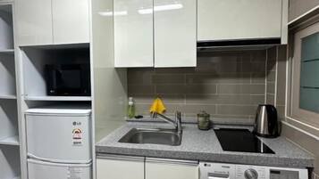 A compact kitchen with white cabinets, a built-in washing machine, and a sink with a kettle.