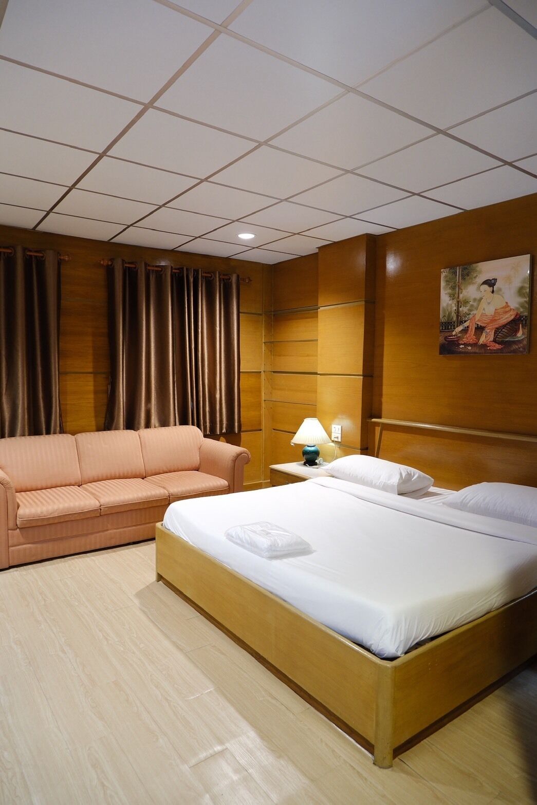 Une chambre d’hôtel avec un lit, un canapé, une table de chevet avec une lampe et un tableau au mur.