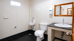 Un baño con orinal, inodoro, lavamanos y espejo.
