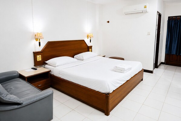 A hotel room with a wooden bed, two bedside lamps, a nightstand, a gray armchair, and a blue curtain.