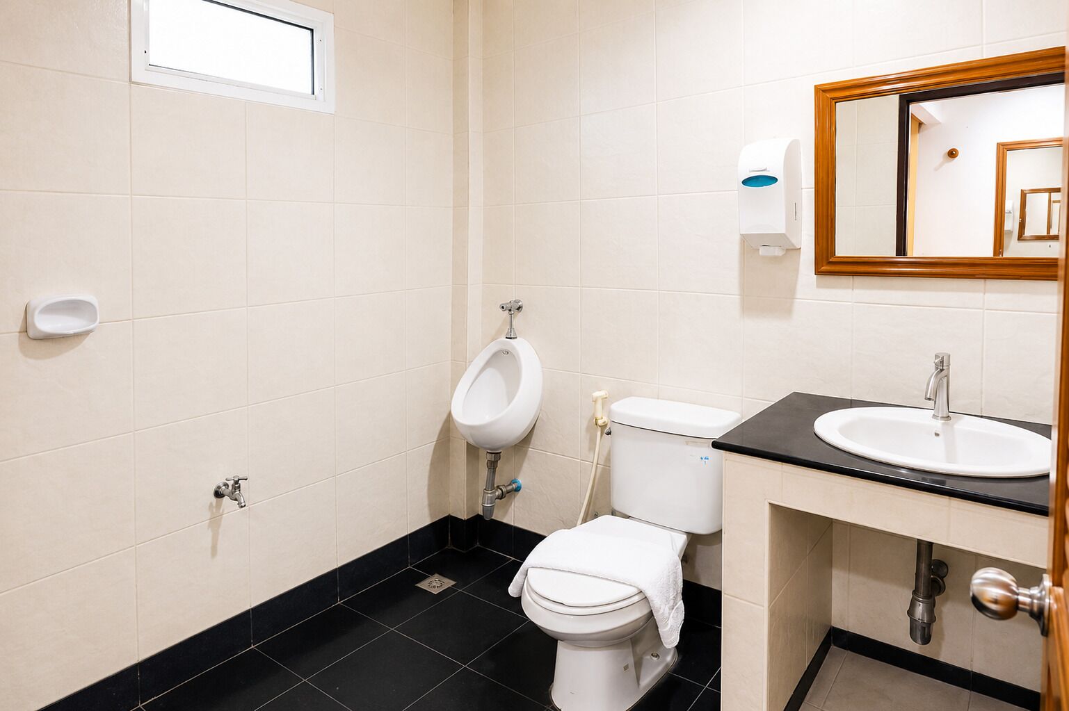 Une salle de bain équipée d’un urinoir, de toilettes, d’un lavabo et d’un miroir.