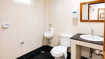 Une salle de bain équipée d’un urinoir, de toilettes, d’un lavabo et d’un miroir.