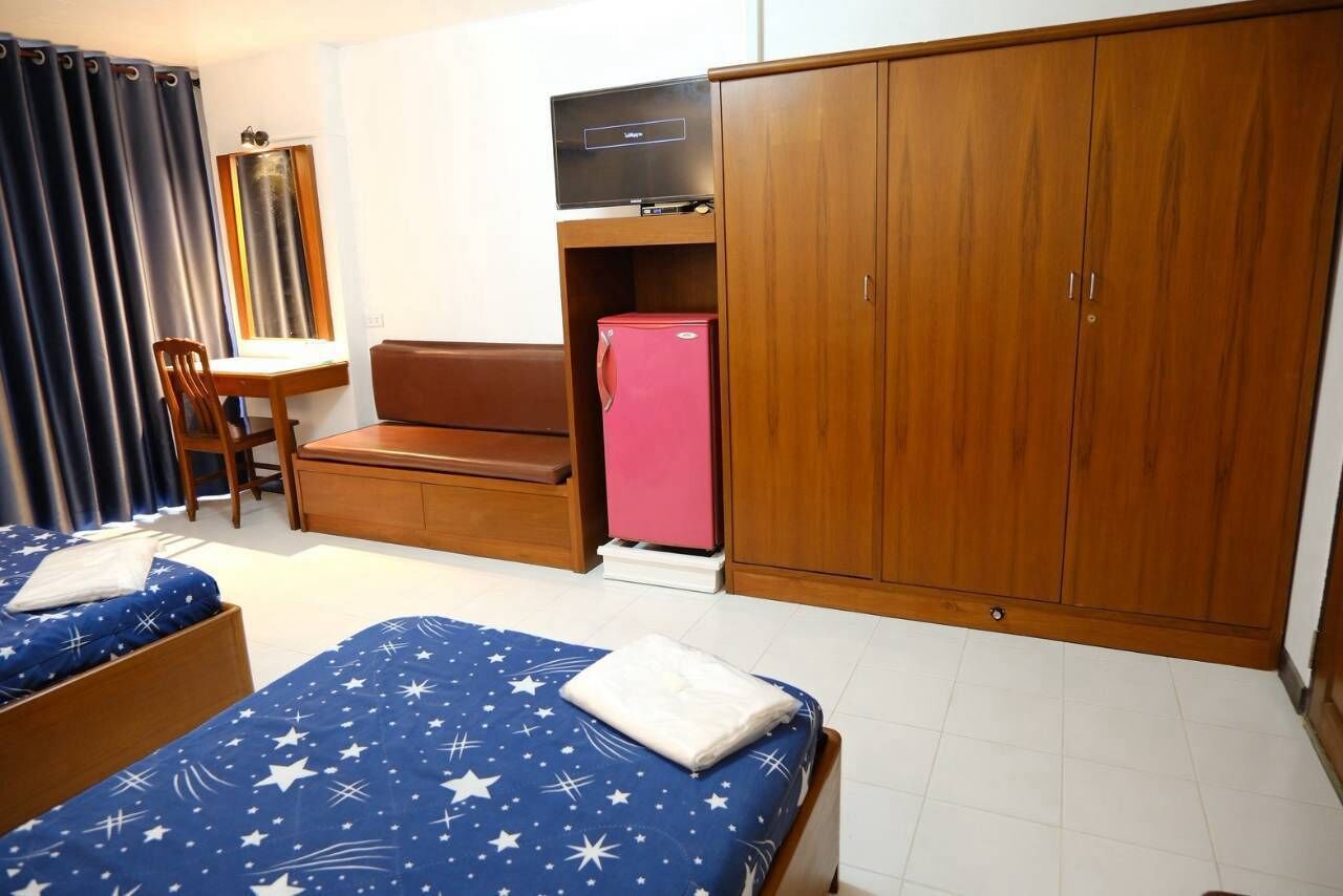 A compact room with two beds, a desk, a chair, a wardrobe, and a refrigerator.
