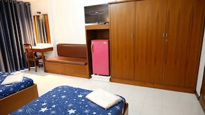 Habitación pequeña con dos camas, un escritorio, una silla, un armario y un refrigerador.