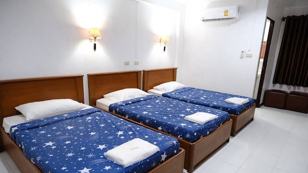 Habitación de hotel con tres camas individuales, cada una con una colcha de estrellas azules y almohadas blancas. Hay lámparas fijadas a la pared a cada lado de las camas.