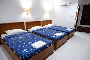 A hotel room with three single beds, each with a blue star-patterned bedspread and white pillows. There are wall-mounted lamps on either side of the beds.