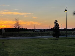 Un atardecer sobre un campo cubierto de hierba, con farolas y un cielo despejado.
