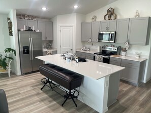 A modern kitchen with grey cabinets, a stainless steel refrigerator, a large island with bar stools, and a microwave above the stove. - Sunset Haven at Crosswind East 3BR Near Disney & Legoland (Haines City)