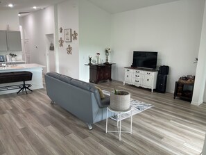 A modern living room with a grey sofa, a white coffee table, and a TV on a white cabinet. - Sunset Haven at Crosswind East 3BR Near Disney & Legoland (Haines City)