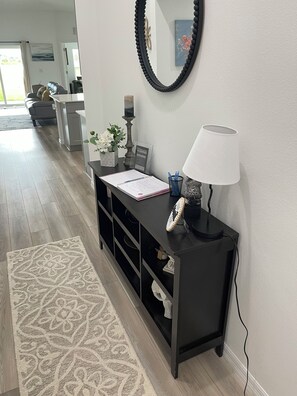 A modern living room with a black console table, a white lamp, and a decorative mirror. - Sunset Haven at Crosswind East 3BR Near Disney & Legoland (Haines City)