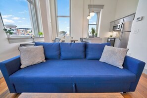 A blue sofa with patterned cushions in a modern living room with large windows and a view of the city. - Modern City Loft - Nearby Parking - Downtown - 2F (Louisville)