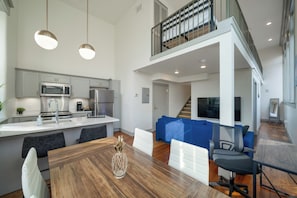 A modern kitchen with stainless steel appliances, a dining area with a wooden table and chairs, and a living space with a blue couch and a TV. - Modern City Loft - Nearby Parking - Downtown - 2F (Louisville)