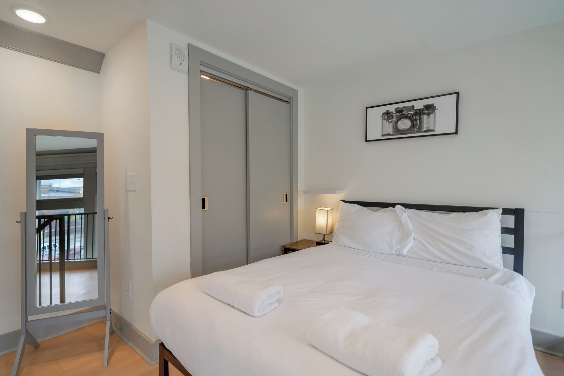 Une chambre d’hôtel avec un lit, une table de chevet avec une lampe, une porte et un tableau encadré au mur.
