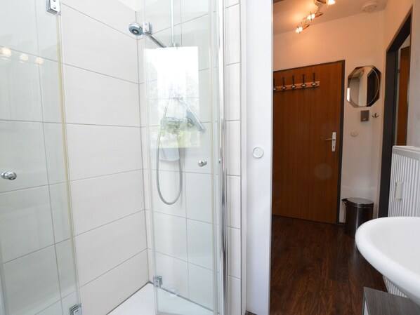 Un baño moderno con cabina de ducha de vidrio, un lavamanos blanco y una puerta de madera.