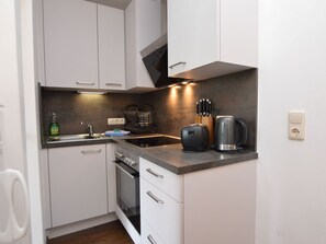 A compact kitchen with white cabinets, a stove, a sink, and a coffee maker. - Cozy apartment, opposite the ski lift. (Hinterthal - Maria-alm)