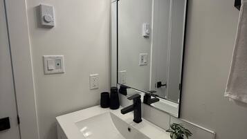 A bathroom with a white sink, black faucet, and a mirror above it. There are three light fixtures above the mirror, and a towel hanging on the wall.