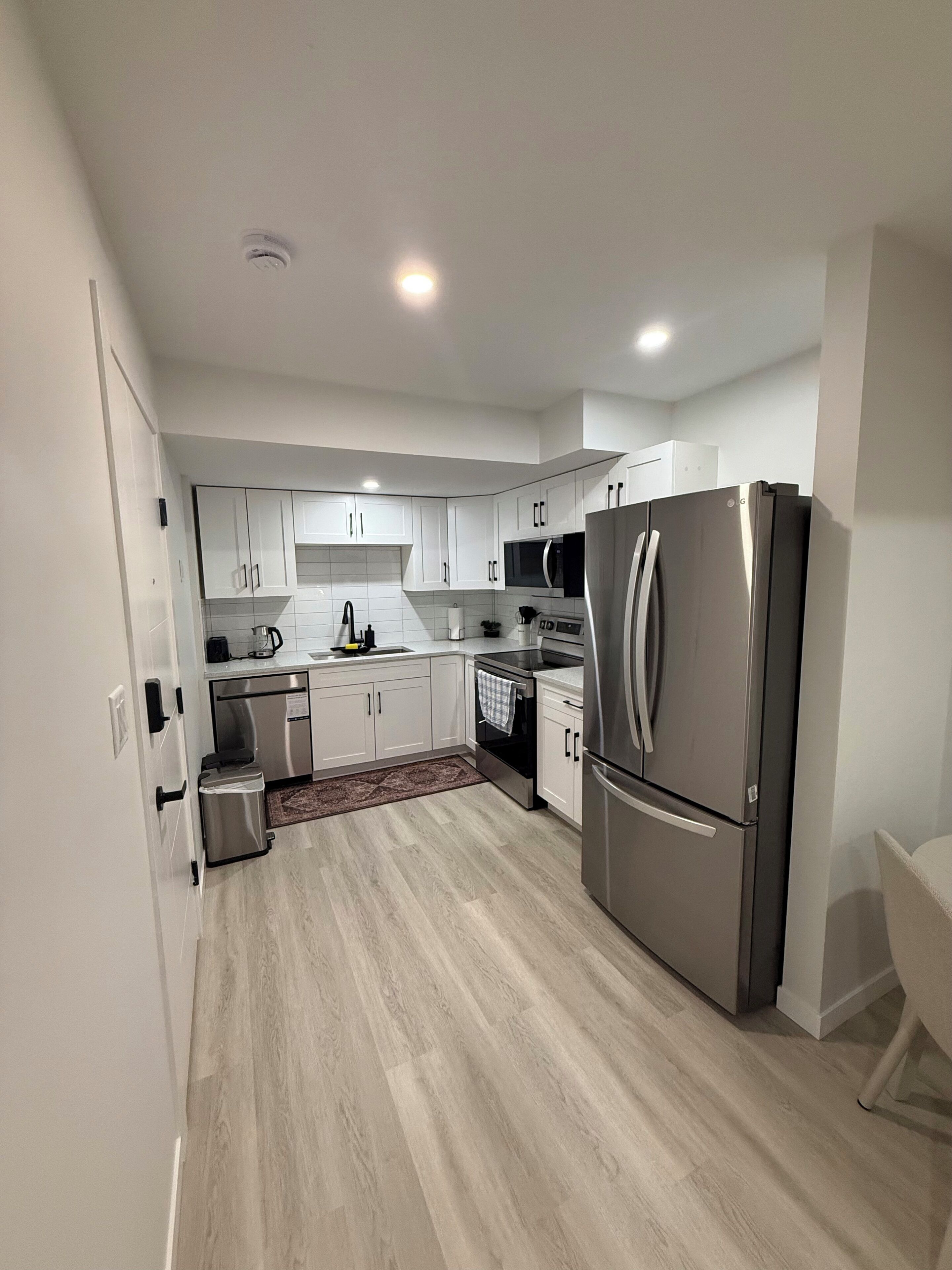 A modern kitchen with white cabinets, stainless steel appliances, and a wooden floor.
