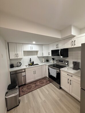 A modern kitchen with white cabinetry, stainless steel appliances, and a tiled backsplash. - Exquisite and modern one bedroom suite (Regina)