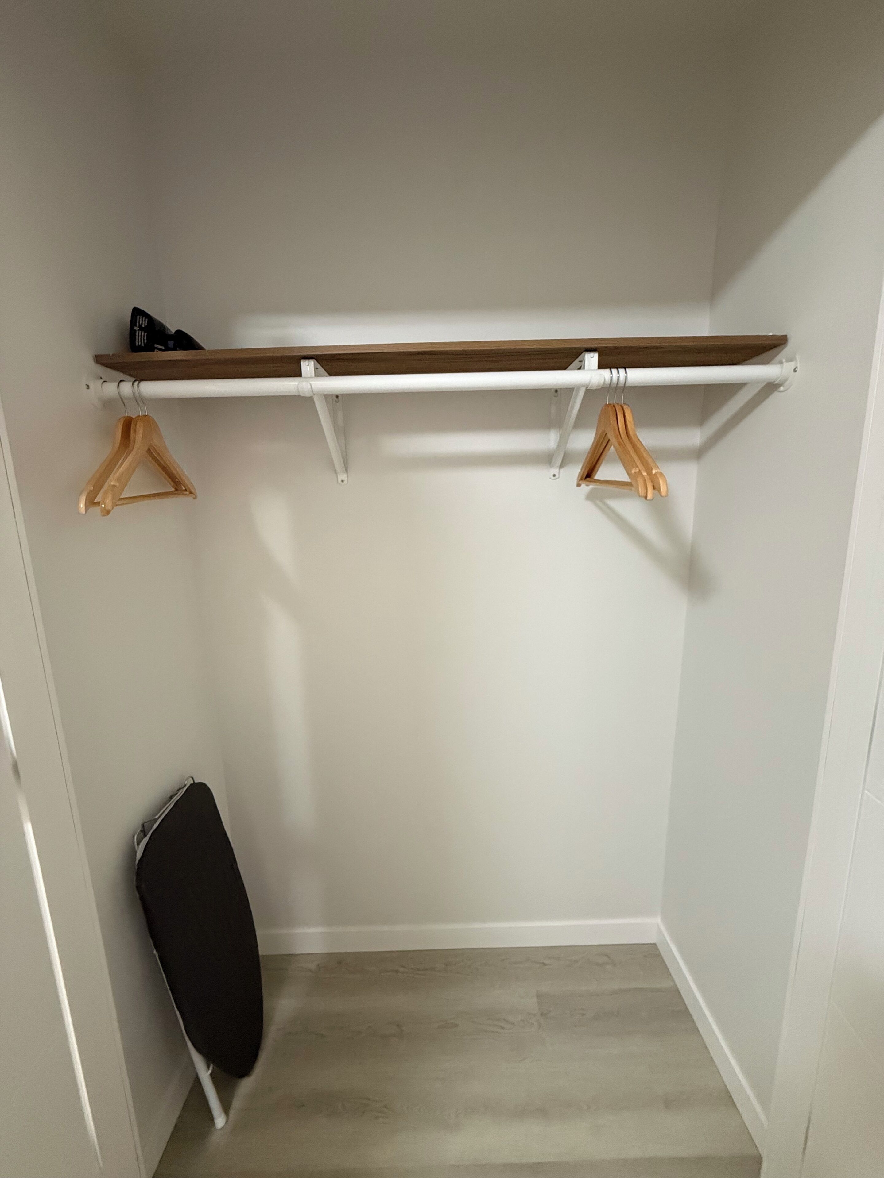 Ein Schrank mit Holzregal, zwei Holzhängern und einem schwarzen Bügelbrett.