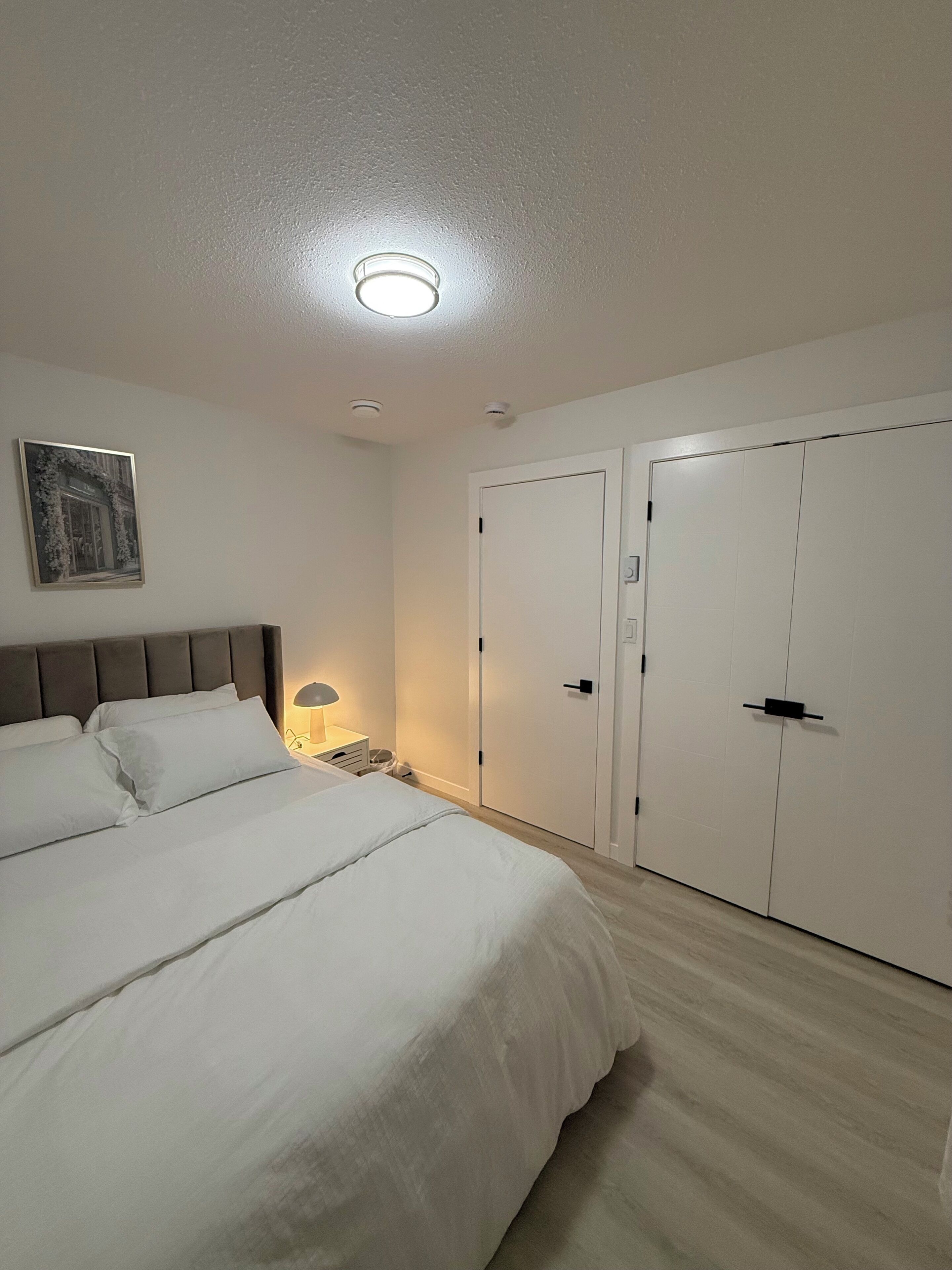 A bedroom with a bed, bedside table, lamp, and two wardrobes.