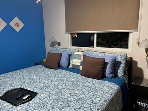 A bedroom with a bed, pillows, a nightstand, a lamp, and a window. - Jaco, Beautiful apartment just a few steps from the ocean, perfect for families. (Jacó)