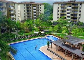 Ein Hotel mit Schwimmbad, umgeben von üppiger Vegetation und einer überdachten Außenlounge.