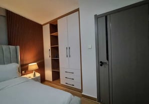 Ein Schlafzimmer mit Bett, Nachttisch, Lampe, Kleiderschrank und einer Tür.