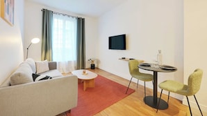 A modern living room with a sofa, a coffee table, a TV mounted on the wall, and a dining area with chairs and a table. - Cosy Appartement - 1bdr/4p - Boulogne Billancourt (Boulogne-Billancourt)