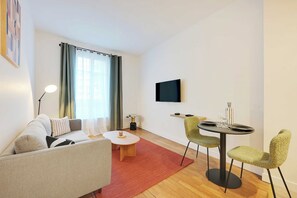 Ein modernes Wohnzimmer mit Sofa, Couchtisch, an der Wand montiertem Fernseher und einem Essbereich mit Stühlen und Tisch.