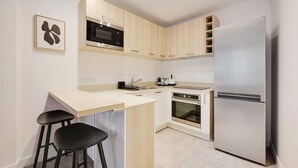 A compact kitchen with a microwave, oven, and refrigerator. There are two stools and a small island with a sink. - Cosy Appartement - 1bdr/4p - Boulogne Billancourt (Boulogne-Billancourt)
