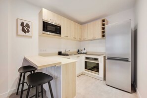 A compact kitchen with a microwave, oven, and refrigerator. There are two stools and a small island with a sink.