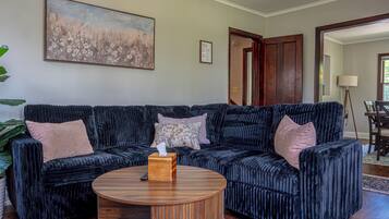 A living room with a dark blue sofa set, a round wooden coffee table, and a floral painting on the wall.