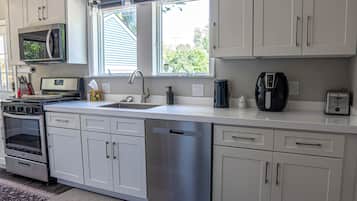 A modern kitchen with stainless steel appliances, a dishwasher, and a window with a view of greenery.
