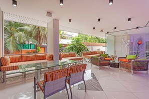 A modern lounge area with glass partitions, striped seating, and a view of greenery outside. - Royal Grand - Luxury 4-bedroom villa for 8 people in Pattaya (Bang Lamung)