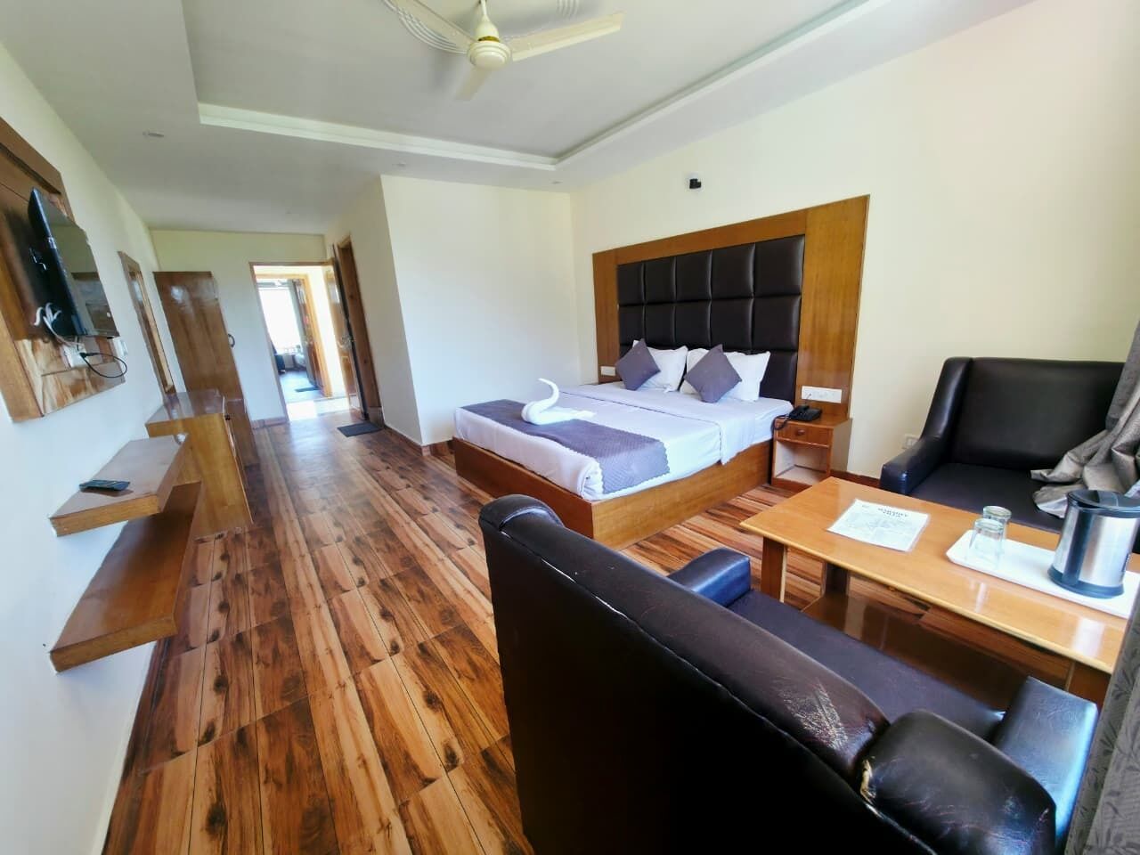 A hotel room with a bed, a desk, a chair, a television, and a ceiling fan.