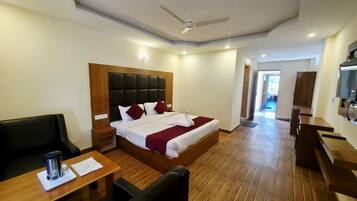 Habitación de hotel con cama, escritorio, silla, televisor y ventilador de techo.