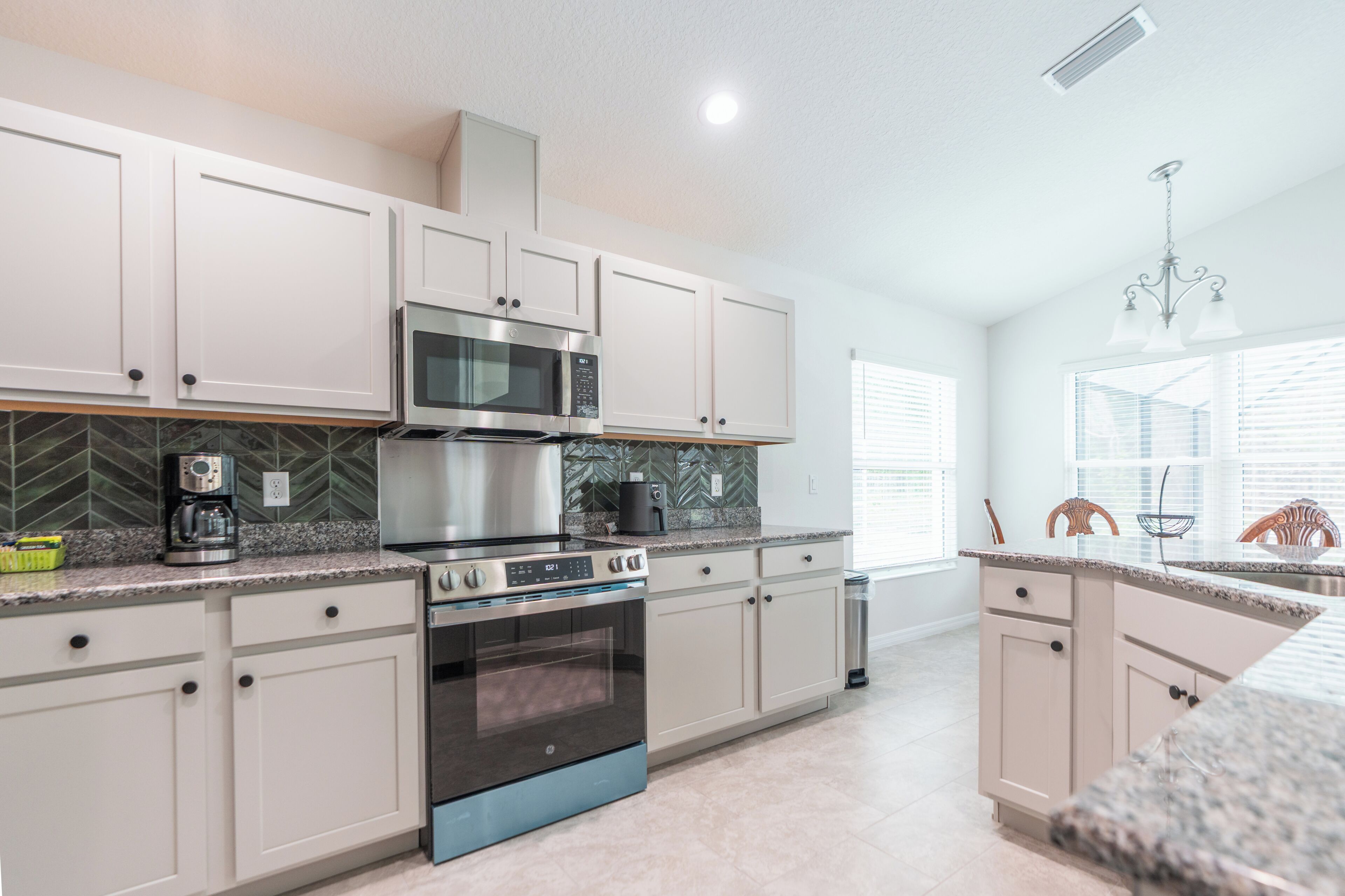 A modern kitchen with stainless steel appliances, white cabinetry, and a herringbone tile backsplash.