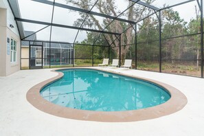 A swimming pool with a glass enclosure, surrounded by a deck with lounge chairs. - Gorgeous, recently remodeled 4-bedroom cozy home with pool near Disney (Kissimmee)