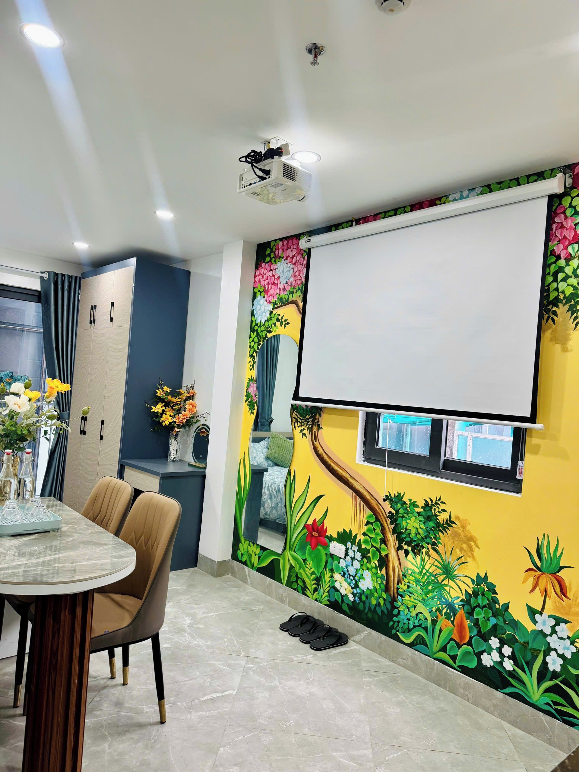 A modern interior with a dining area, a projector screen, and a mural with floral and tree designs.