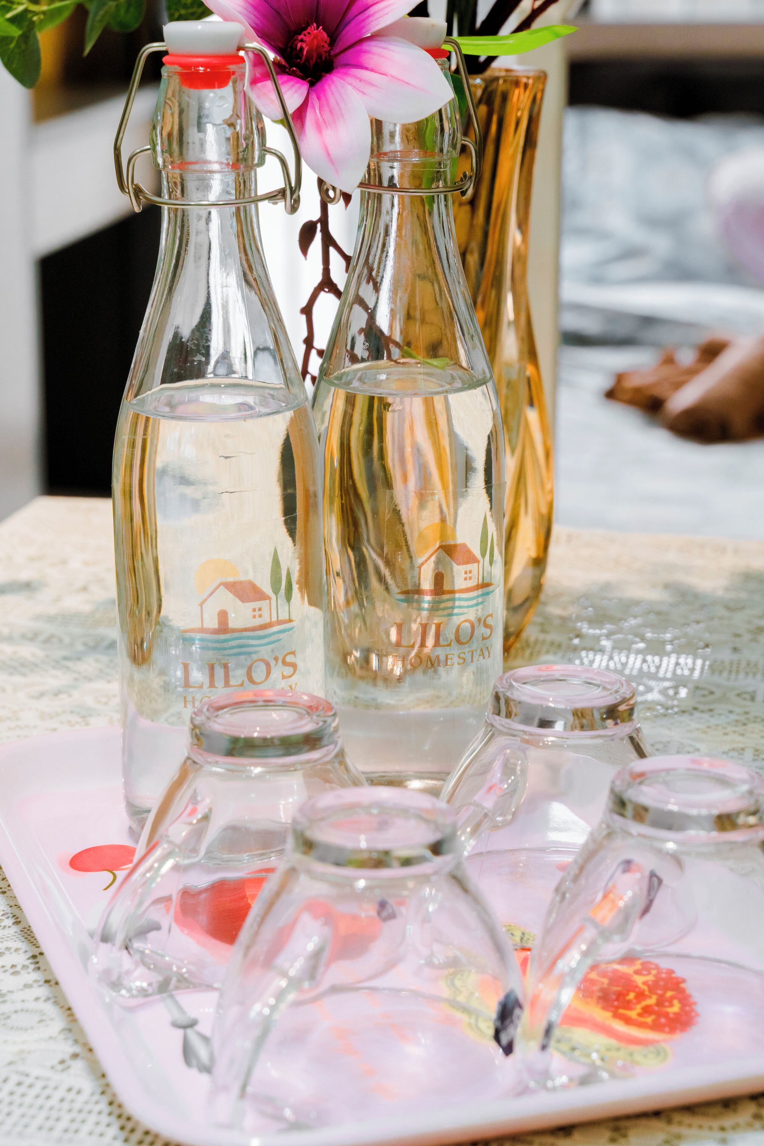 A tray with multiple glass bottles and a vase with a flower.