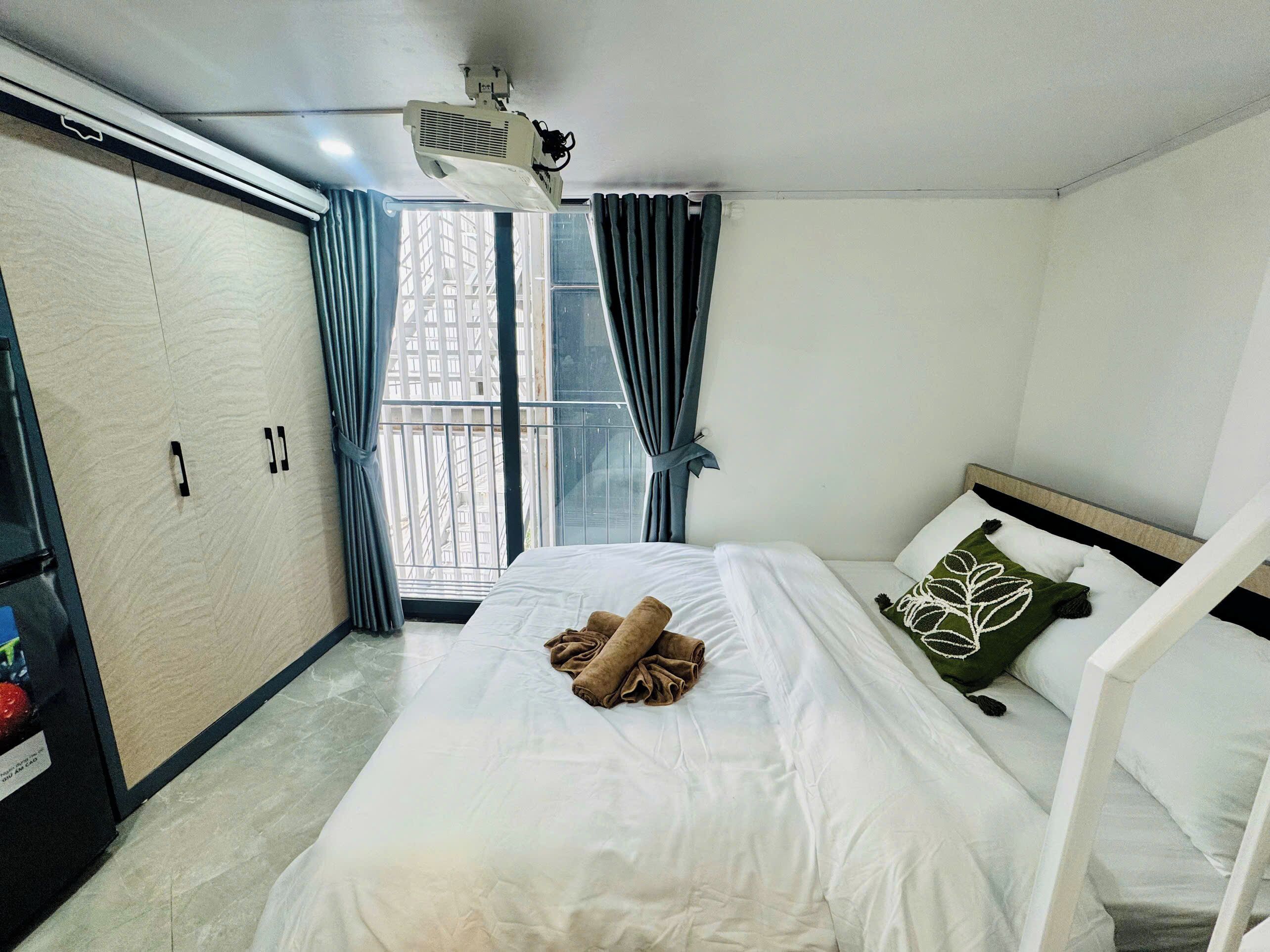 A hotel room with a bed, a projector, a window with curtains, and a view of the outside.