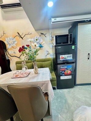 A dining area with a table set for two, a vase with flowers, and a refrigerator with a Funiki label.