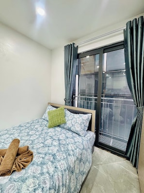 A hotel room with a bed, a window with curtains, a radiator, and a view of the outside.