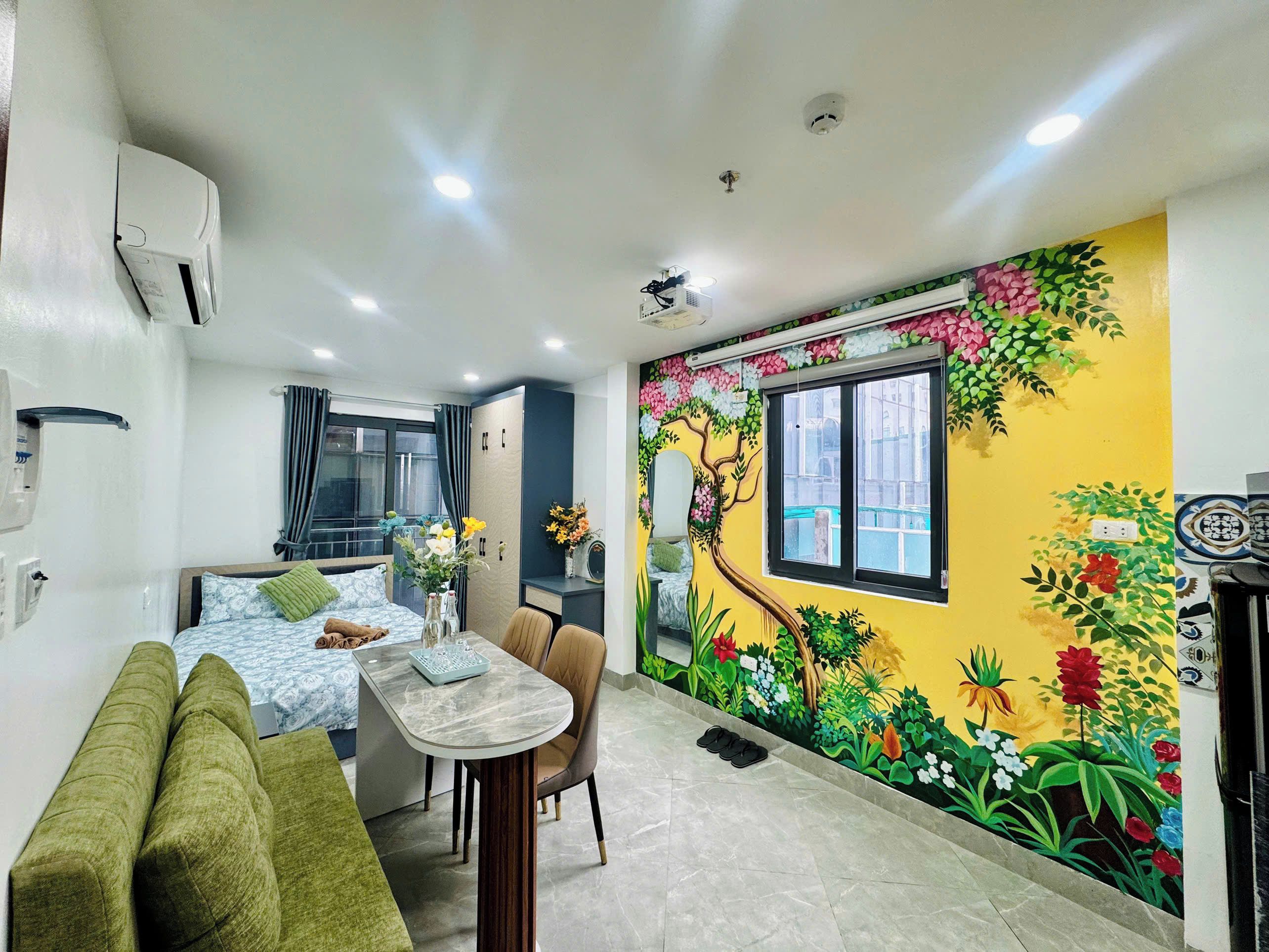 Une chambre d’hôtel comprenant un lit, un canapé, une table à manger avec des chaises, un petit coin cuisine et une fresque colorée sur le mur.