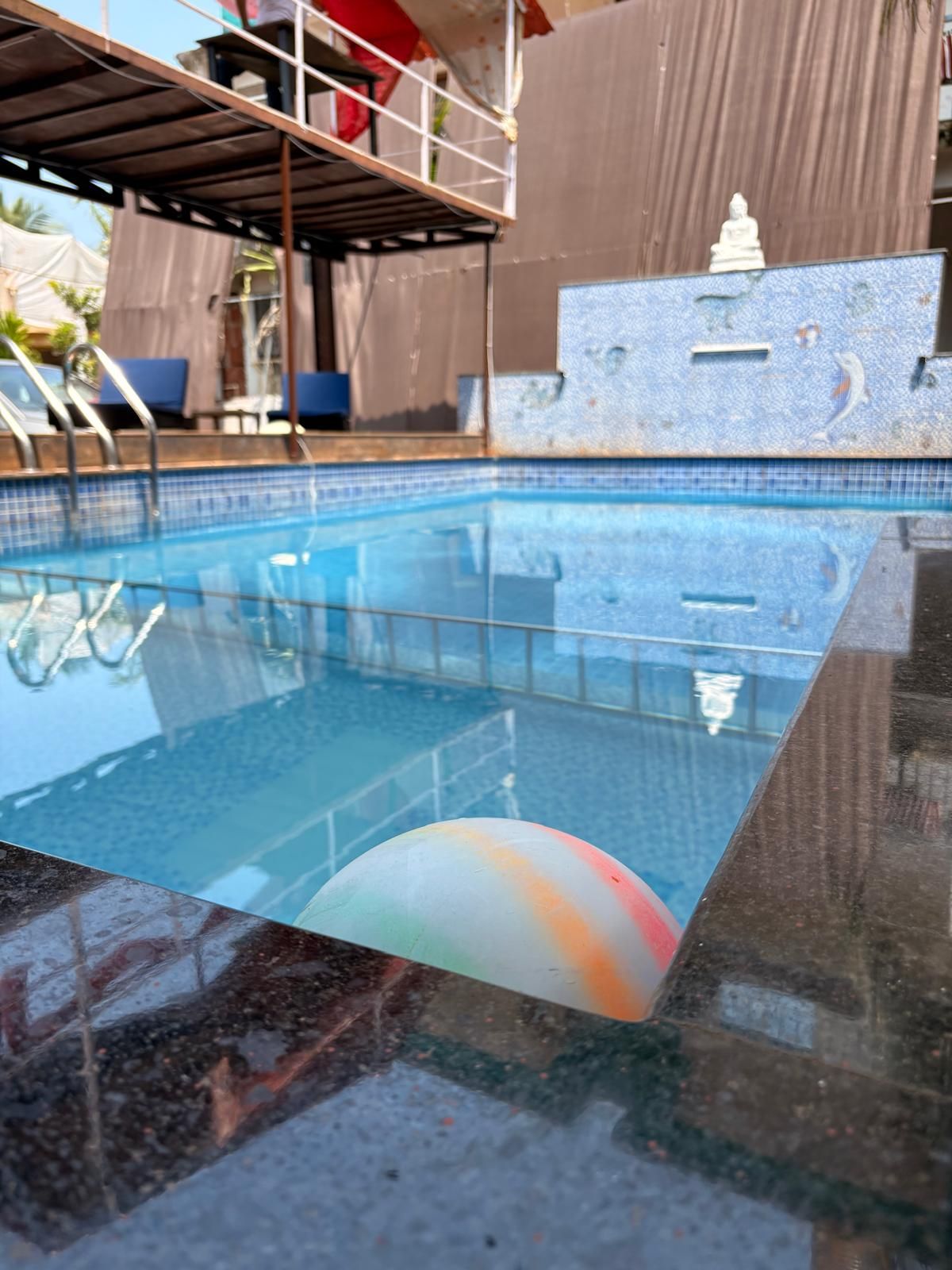 Una piscina con agua cristalina, una pared azulejada con una estatua y un área de descanso cubierta.