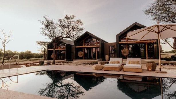 A modern house with a swimming pool, outdoor seating, and a large umbrella.