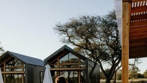 A person walking on a stone pathway towards a building with a modern design, surrounded by outdoor seating and a pergola.